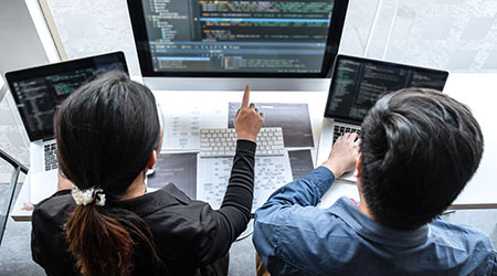 Man and woman working in their computers with a monitor in between