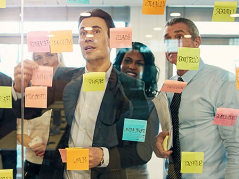 3 men in suit looking at an agile board with sticky notes
